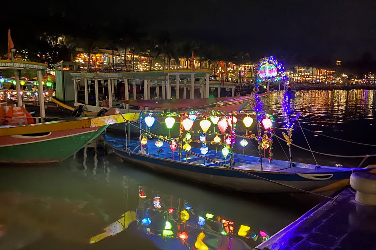 Hoi An Ancient Town at dusk — silk lanterns hanging above the old quarter, the Japanese covered bridge lit up, wooden shophouses reflected in the Thu Bon river. UNESCO World Heritage 1999.